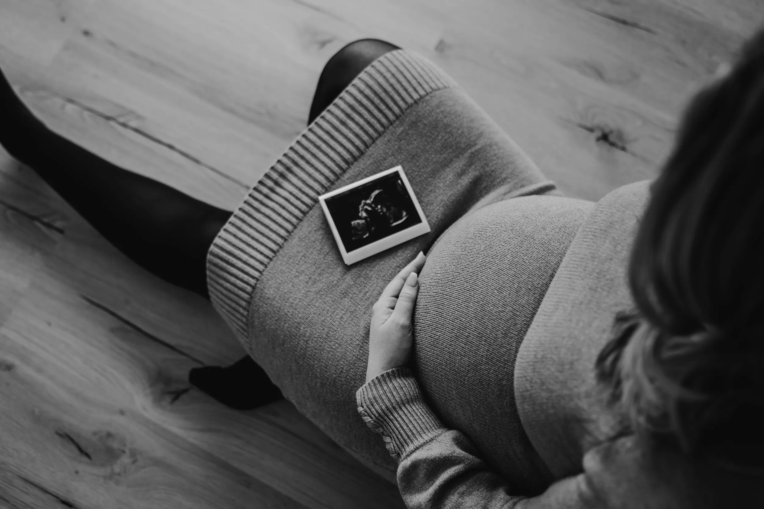 Frau hält Babybauch mit Ultraschallfoto auf dem Schoß