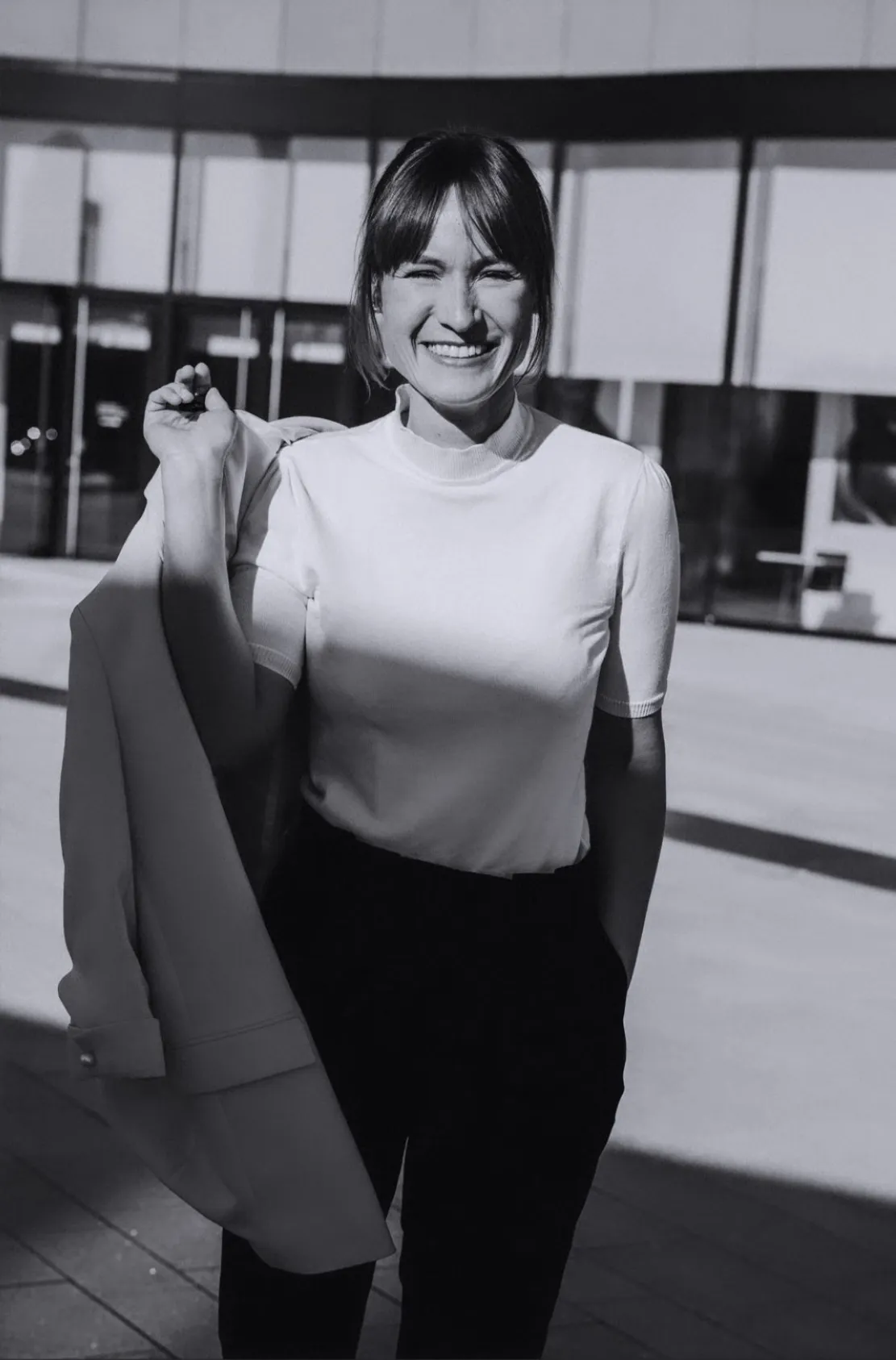 Frau in Business Outfit spaßt lässig mit Blazer über der Schulter