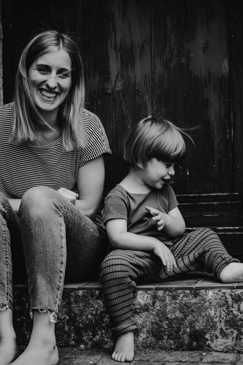 Mutter sitzt mit Sohn lachend draußen auf Treppenstufe