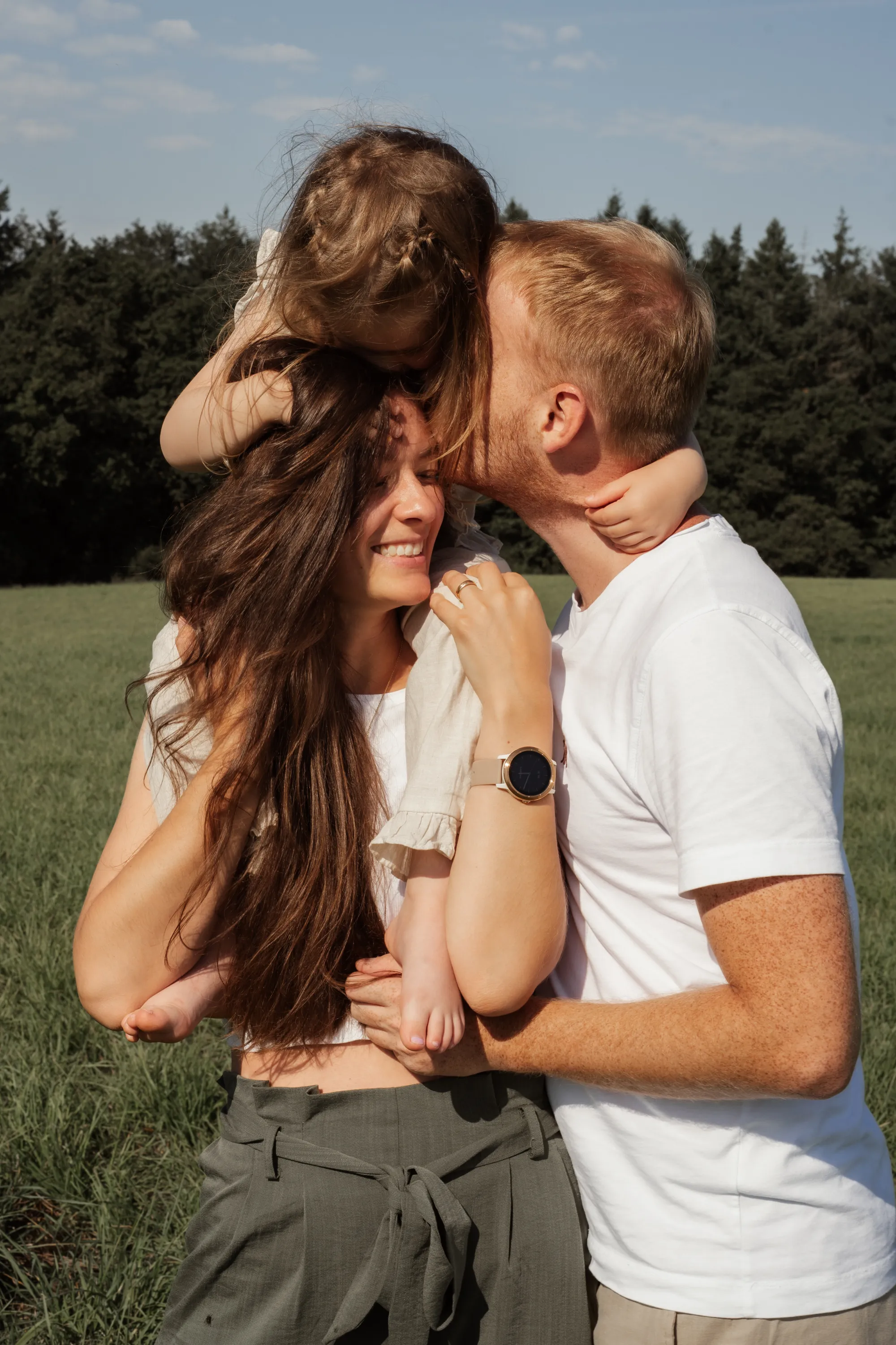 Junge Familie mit Tochter auf den Schultern der Mama auf sonniger Wiese