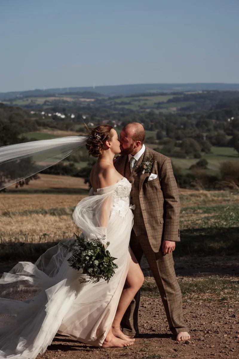 Brautpaar steht barfuß in starker Windböe und küsst sich