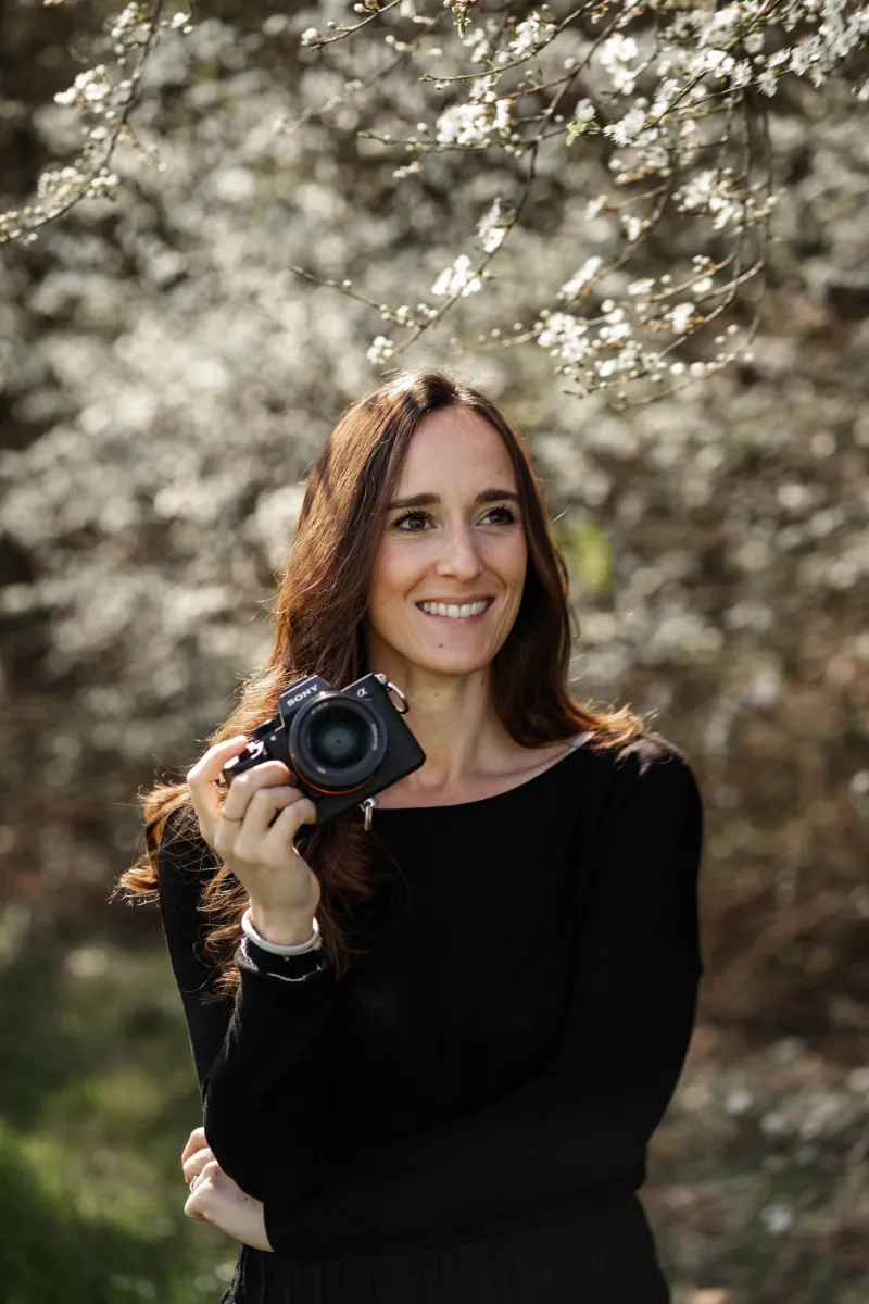 Jacky unter blühendem Kirschbaum lächelt mit Kamera in der Hand