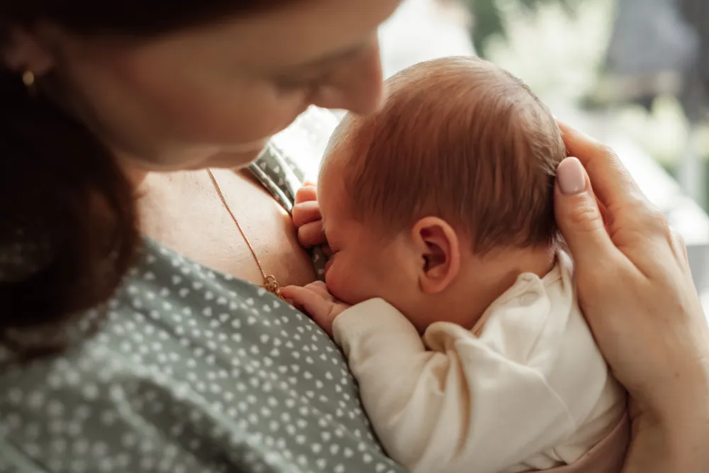 Mutter hält ihr Neugeborenes auf der Brust und stützt das Köpfchen