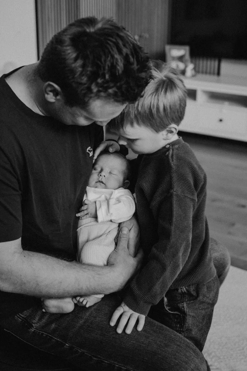 Großer Bruder bewundert Geschwisterchen bei Papa im Arm